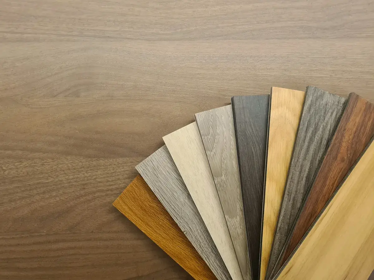 A fan of vinyl plank samples laid out on a wood surface, in oak, ash, weathered grey and dark walnut finishes.